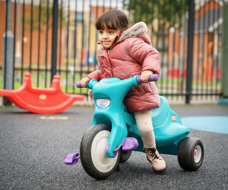 A young child riding a tricycle in a playground. 