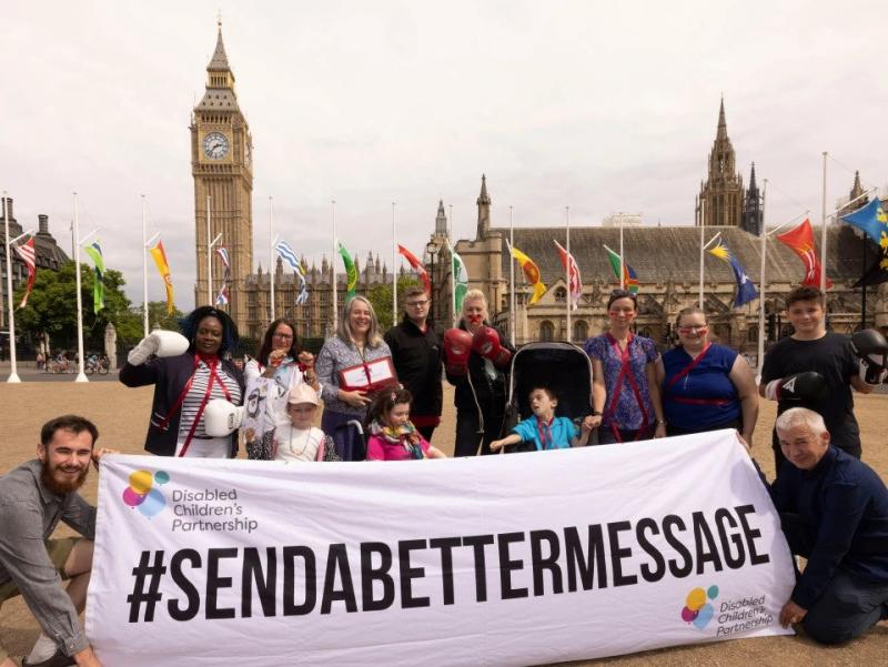 A group of parents and disabled young people standing outside parliament with a banner that says #SENDABetterMessage.